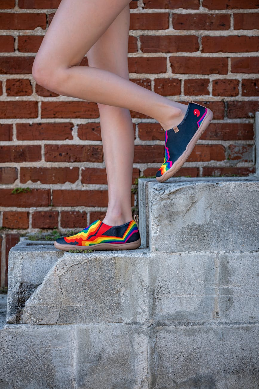 a woman in colorful shoes standing on a brick wall